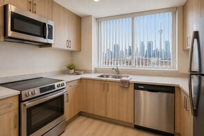 Eine moderne Küche mit Edelstahlgeräten, Holzschränken, einem großen Fenster mit Blick auf die Stadt und einem Geschirrspüler.