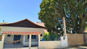 A house with a tiled roof, a fenced yard, and a large tree. - Grandma's house in Piúma: Backyard, Porch and 3 Bedrooms (Piúma)