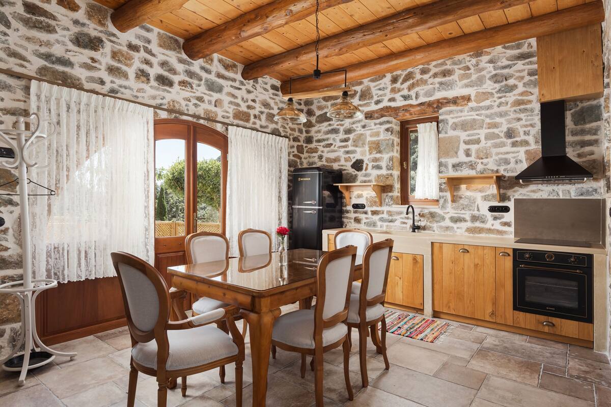 Una cocina con paredes de piedra, armarios de madera, una mesa de comedor con sillas, un refrigerador y un horno.