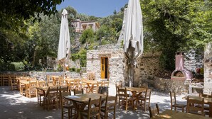 An outdoor seating area with stone walls, wooden tables and chairs, and a stone oven. - Manelis Mills Estate - Guest Houses (Myrthianos Plakias)