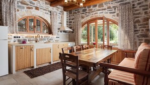 A rustic kitchen with stone walls, wooden furniture, and large windows. - Manelis Mills Estate - Guest Houses (Myrthianos Plakias)