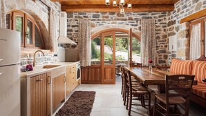 A rustic stone kitchen with wooden cabinets, a dining area with a wooden table and chairs, and a stone wall. - Manelis Mills Estate - Guest Houses (Myrthianos Plakias)