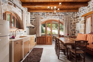 Une cuisine rustique avec des murs en pierre, des armoires en bois, un coin repas avec une table et des chaises en bois, et un mur en pierre.