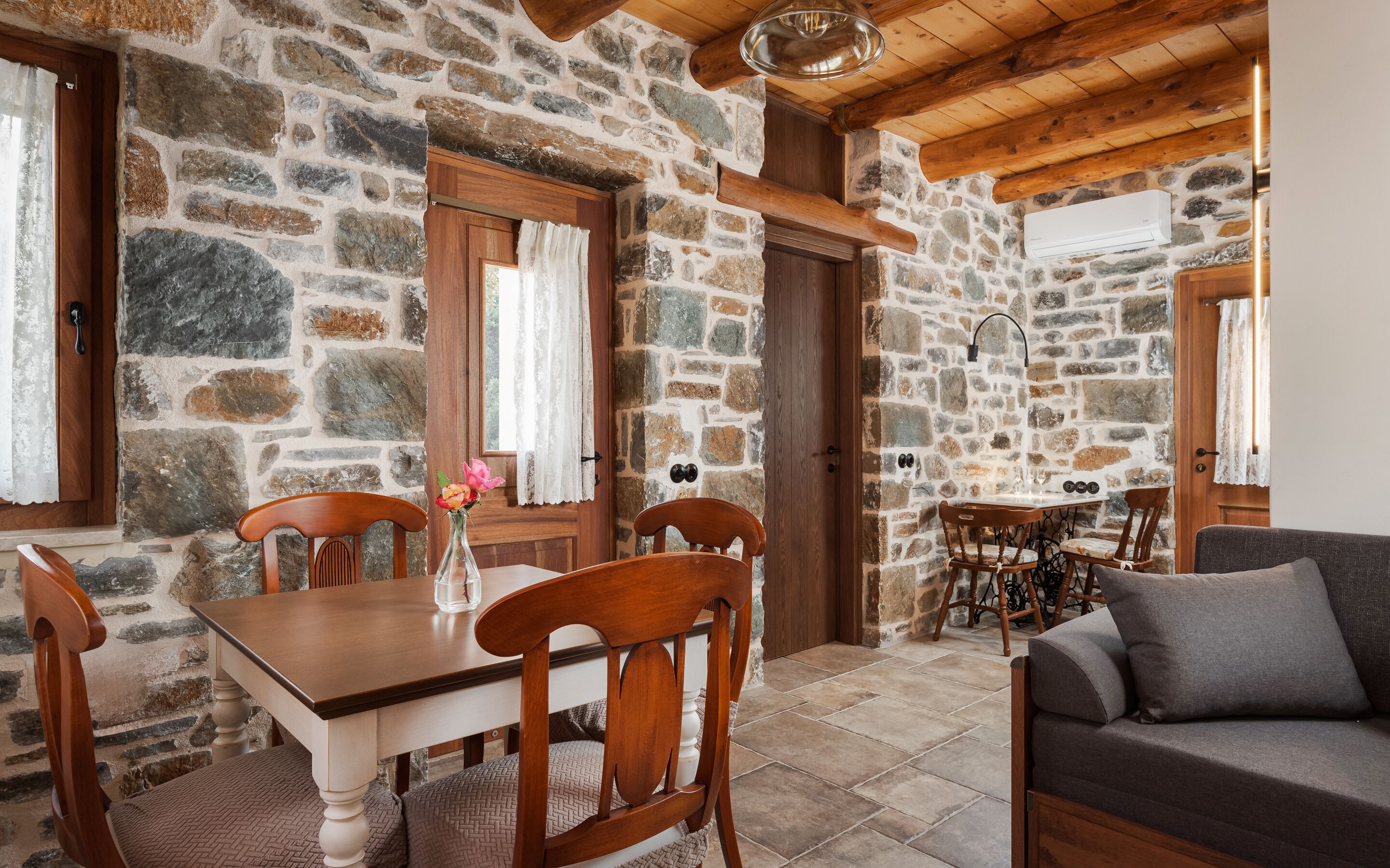 A stone-walled room with a wooden dining table, chairs, and a sofa.
