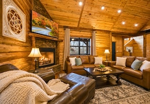 A log cabin interior with a fireplace, leather sofas, a television, and a large window. - Trails Nearby | Fire Pit | Hot Tub | Covered Deck (Broken Bow)