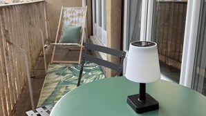 Un balcón con una mesa verde y una silla, una ventana y vistas a edificios.