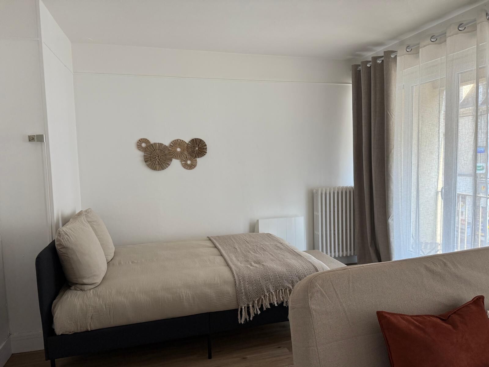 Een slaapkamer met een bed, een radiator en een raam met gordijnen.