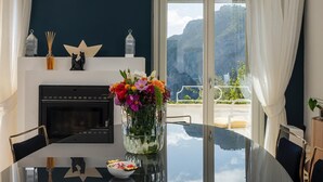 Ein moderner Essraum mit Glastisch, Kamin, Blumenvase und Balkon mit Bergblick.