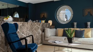 Ein modernes Wohnzimmer mit blauem Sessel, einer Couch, einem runden Tisch und einem großen Spiegel.