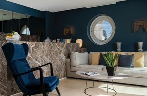 A modern living room with a blue armchair, a sofa, a round table, and a large mirror.