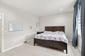 A bedroom with a bed, a nightstand, a mirror, and a window with curtains. - Spacious Modern Calgary Home | 3 Bedrooms + 2 Bonus Rooms (Calgary)