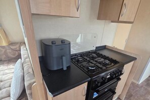 A compact kitchenette with a gas stove, a coffee maker, and wooden cabinets.