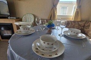 A dining table set with white dishes featuring bee patterns, surrounded by chairs and a small vase with blue flowers.