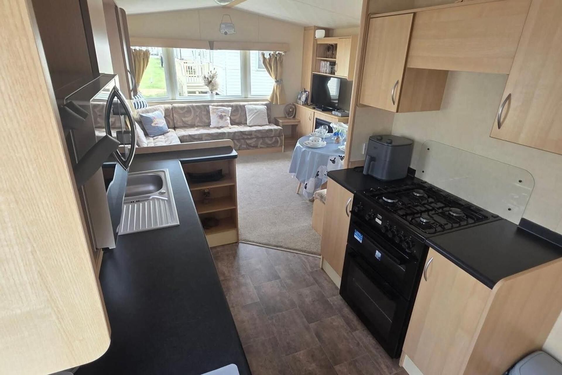 A compact RV kitchen with a stove, sink, and a dining area with a table and chairs.