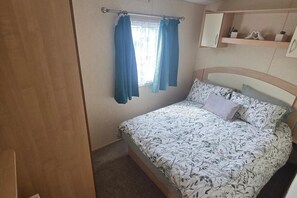 A bedroom with a bed, curtains, a mirror, and a shelf with decorative items.