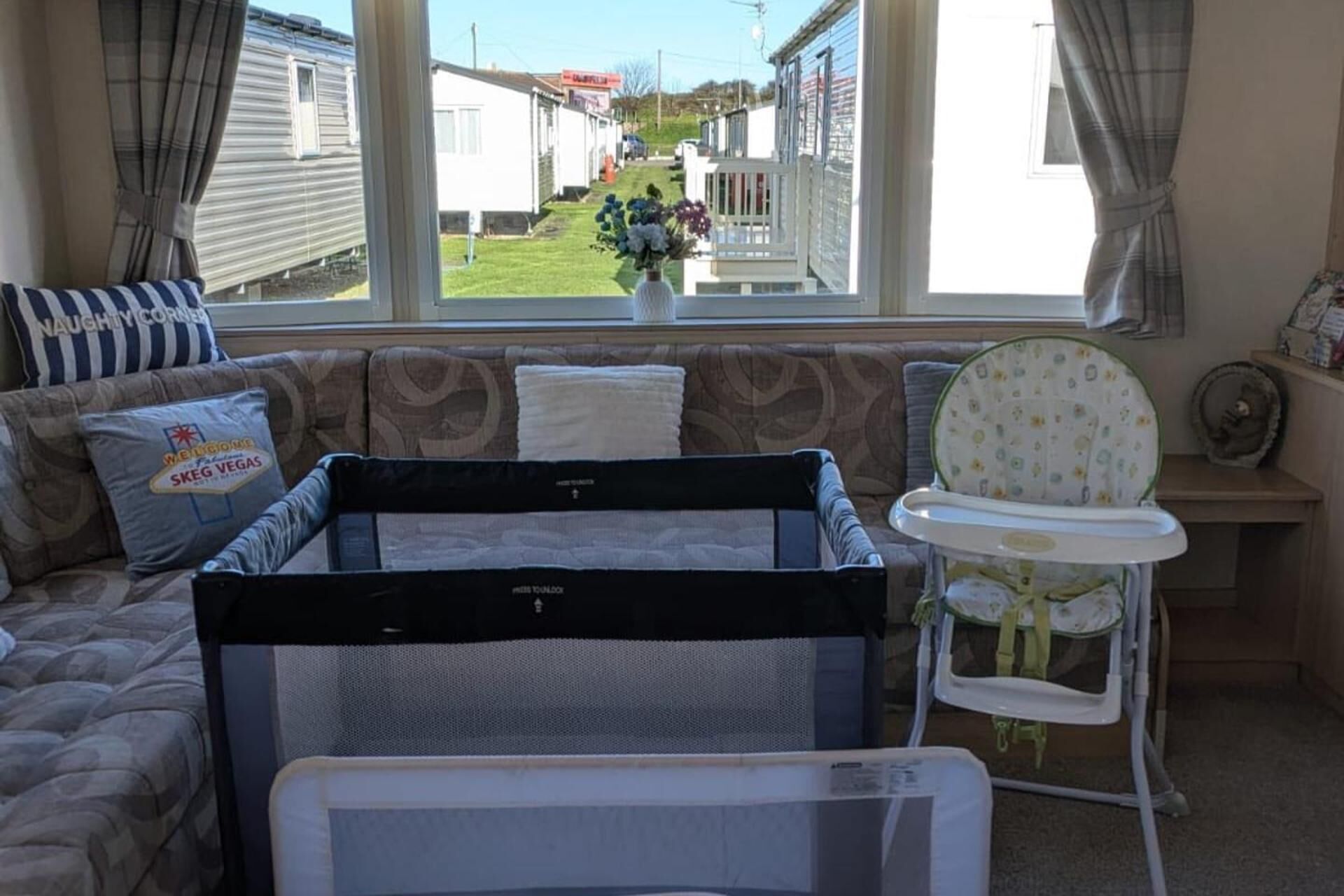 A room with a bed, a window with a view of mobile homes, a baby crib, and a high chair.