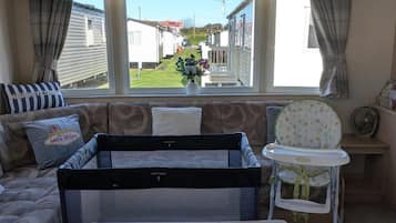 A room with a bed, a window with a view of mobile homes, a baby crib, and a high chair.