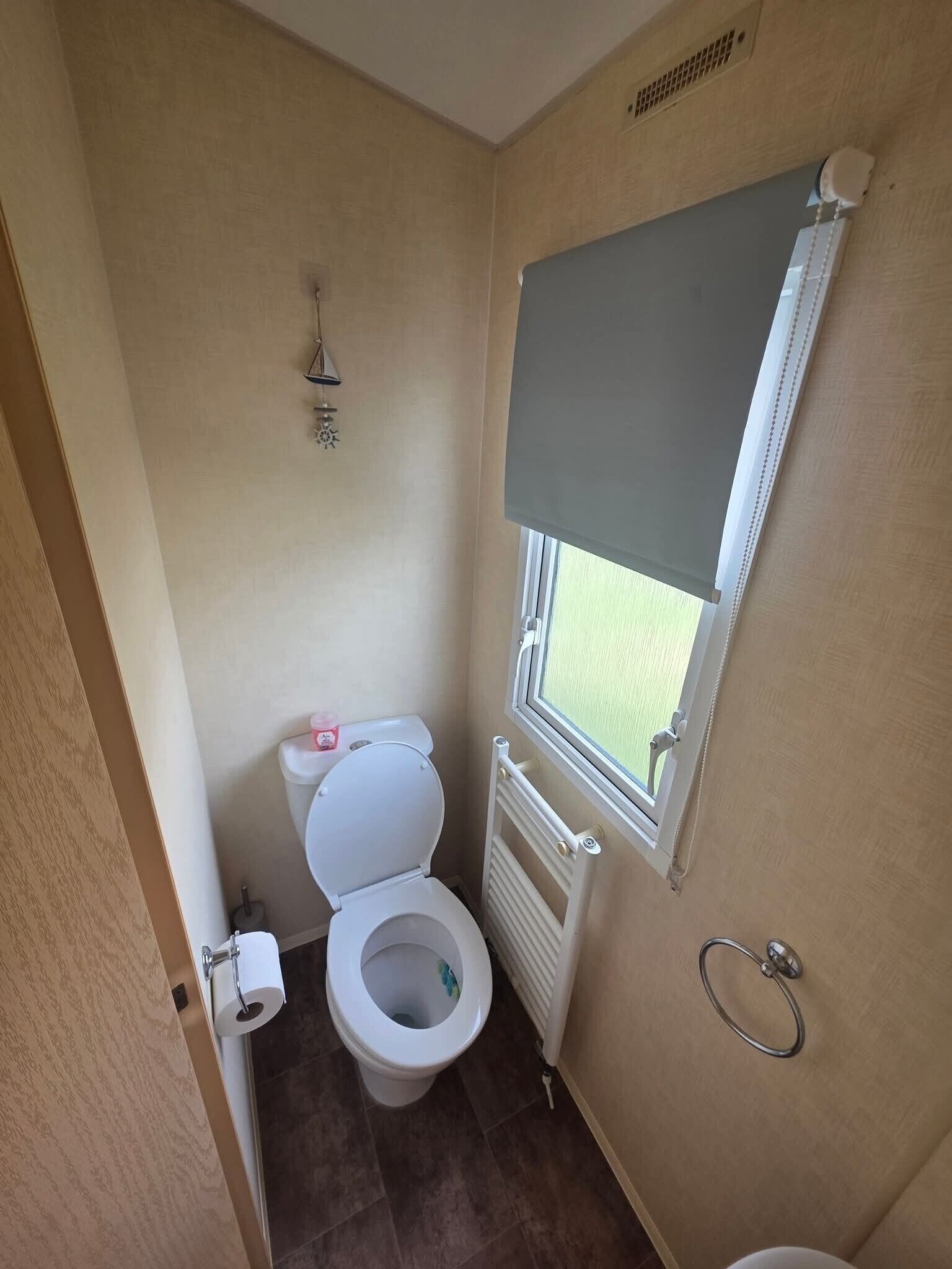 A compact bathroom with a toilet, a radiator, a window, and a towel rack.