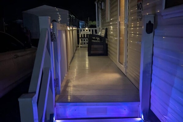 A covered outdoor area with a wooden deck, a white railing, and a bench.