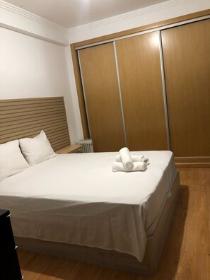 Ein Hotelzimmer mit Bett, Holz-Kopfteil, großem Kleiderschrank und Heizkörper.