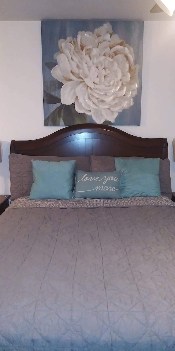 A bed with a patterned bedspread, two pillows with text, and a large floral artwork above.
