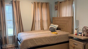 Ein Schlafzimmer mit einem Bett, einem Nachttisch, einem Sessel, einem Fenster mit Vorhängen und einem Teppich.