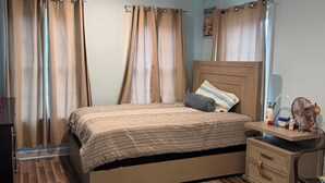 Ein Schlafzimmer mit Bett, Vorhängen, Nachttisch, Teppich und einem Sessel.