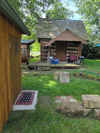A rustic cabin with a stone exterior, a wooden porch, and a small outdoor seating area.. Charming 1-bedroom cabin in Medina perfect for a cozy getaway