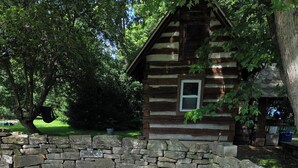 Uma cabana rústica de toras com parede de pedra e entrada por um caminho de cascalho.