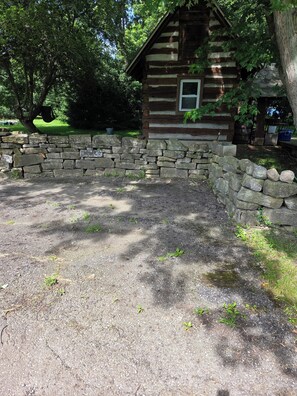 Une cabane rustique en rondins de bois, dotĂ©e dâun mur en pierre et dâune allĂ©e gravillonnĂ©e.