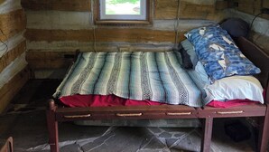 Quarto de cabana de toras com uma cama, janela e piso de pedra.
