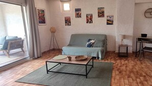 A living room with a sofa, a coffee table, a wicker chair, a desk, and a lamp. - A haven of peace. Ground floor of a villa near the harbor with a private garden and entrance (Sanary-sur-Mer)