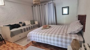 A bedroom with a bed, a sofa, a small table, a window with curtains, and a wall-mounted picture frame. - A haven of peace. Ground floor of a villa near the harbor with a private garden and entrance (Sanary-sur-Mer)