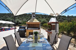 Un espace extérieur aménagé pour les repas, avec un barbecue en briques, un gril et une table pour quatre personnes.
