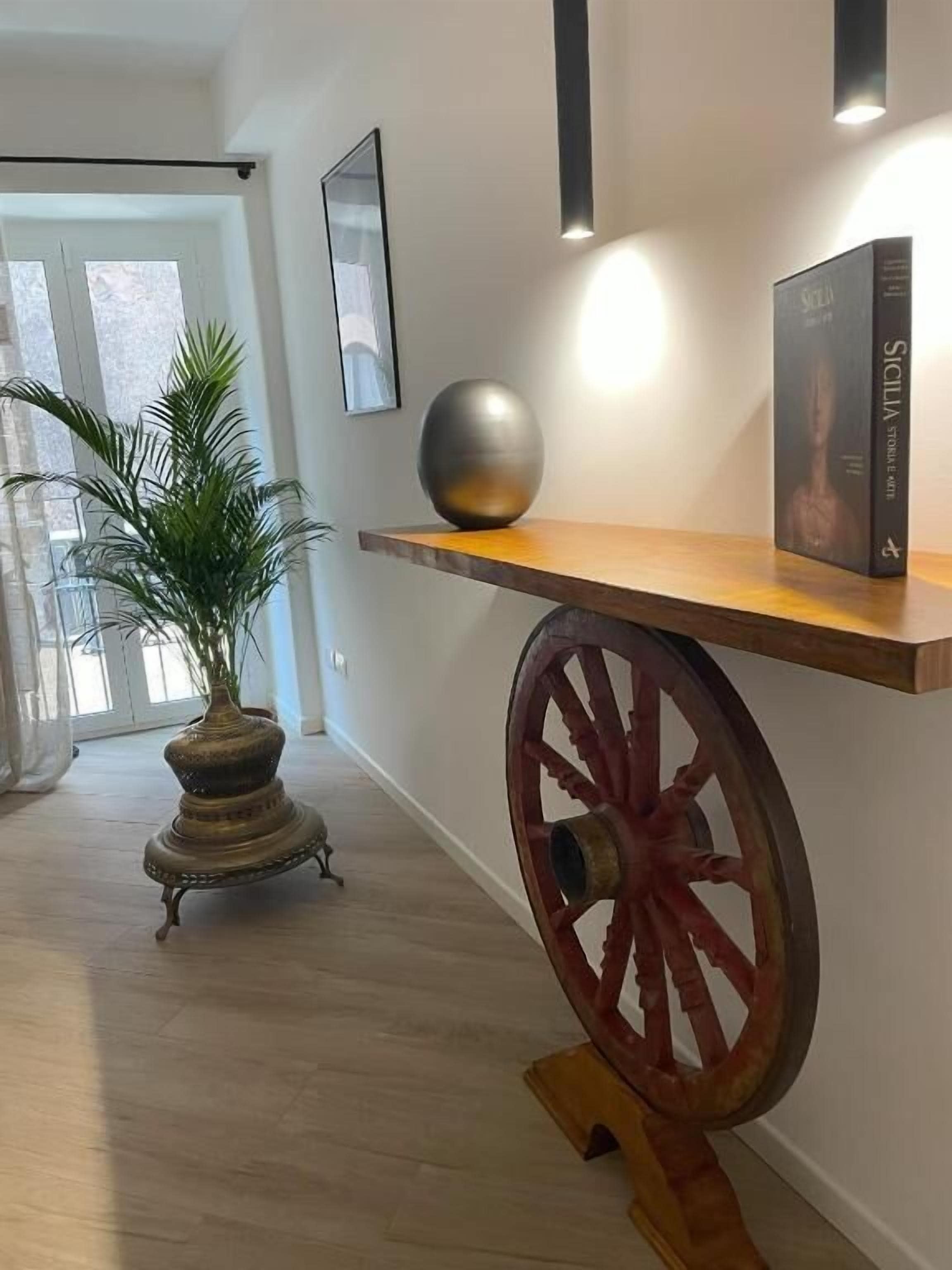 A hallway with a wooden shelf, a decorative wheel, and a potted plant.