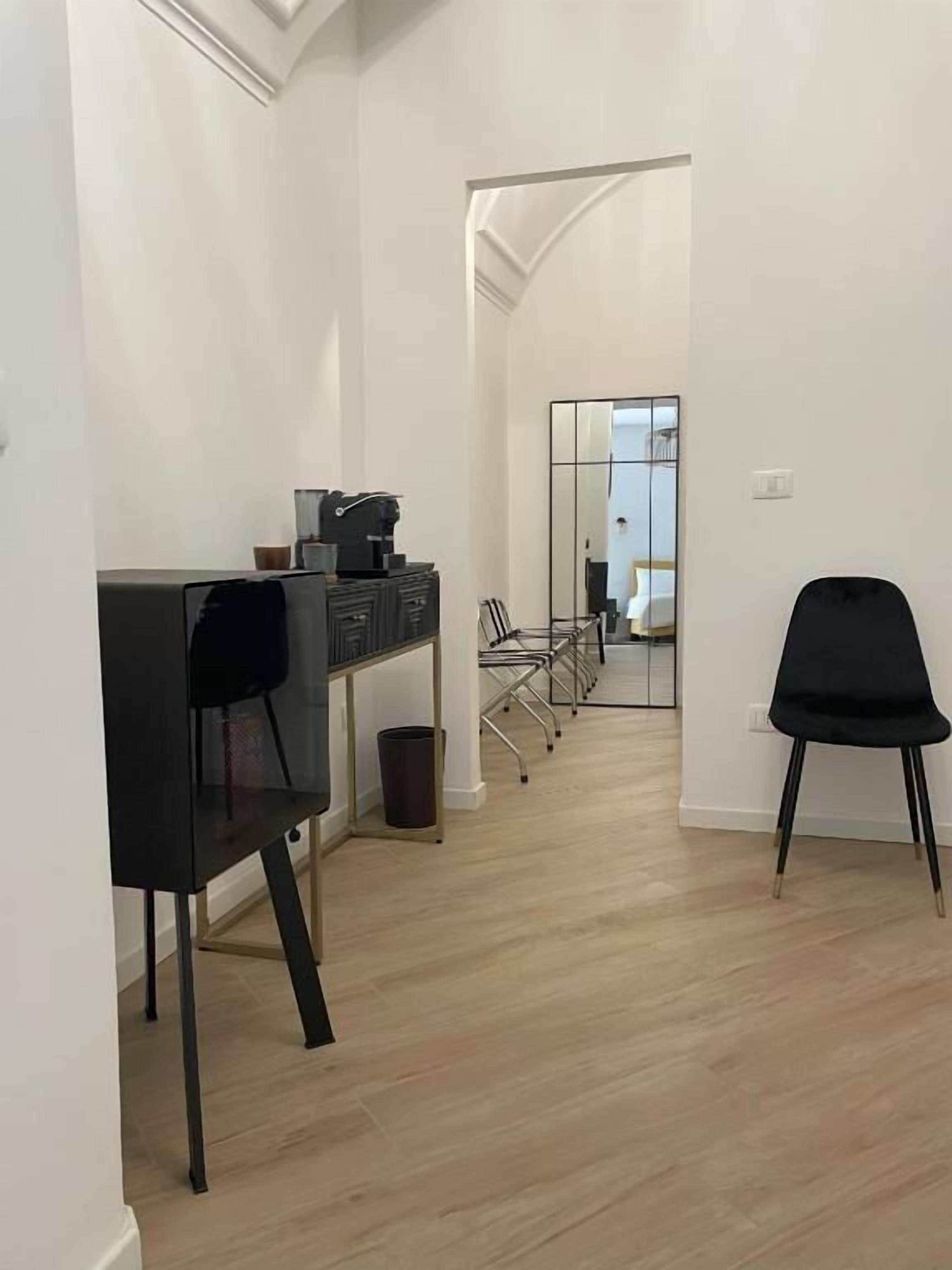 A modern interior with a long hallway, a desk with a chair, and a large mirror reflecting the room.