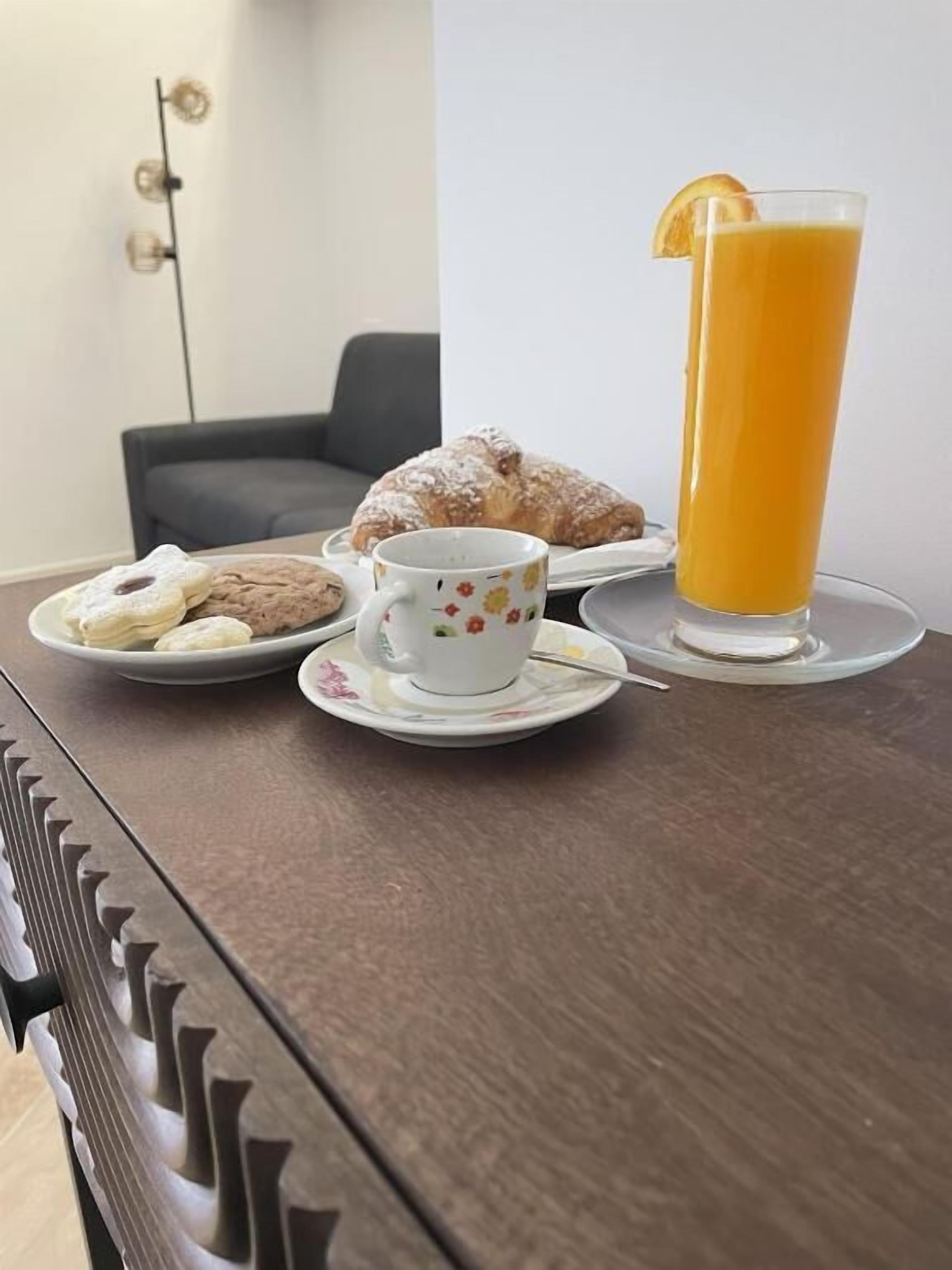 Una mesa con un plato de galletas, una taza de té y un vaso de zumo de naranja.