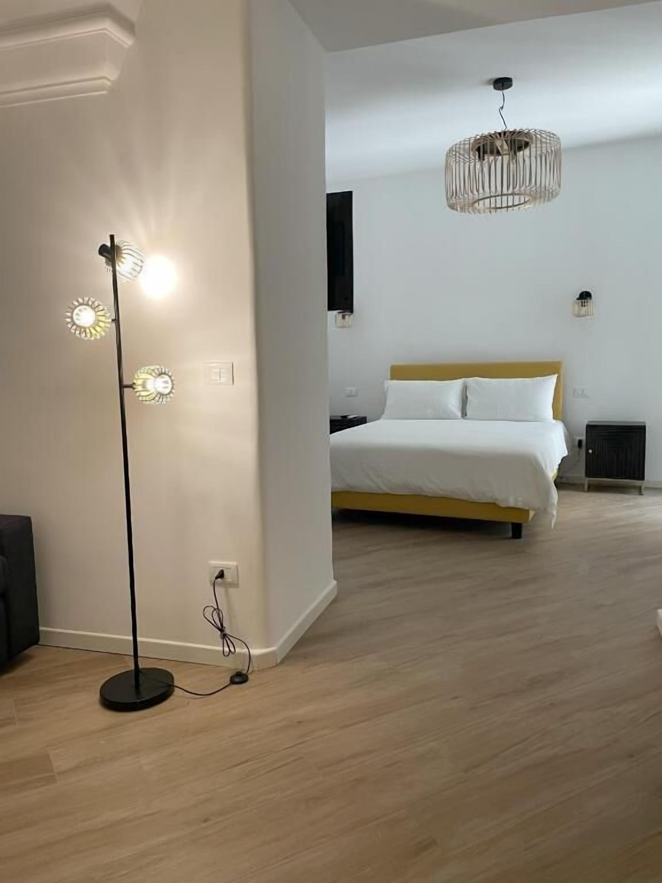 A bedroom with a bed, a floor lamp, and a hanging light fixture.