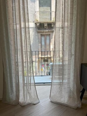 A room with sheer curtains, a balcony, and a view of a building outside. - Ca' Semu (Catania)