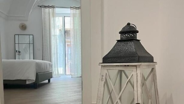 Käytävä, jossa on valkoinen lyhty, puulattia ja taustalla näkyy sänky.