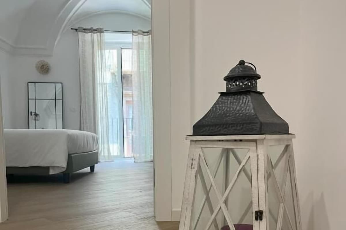 A hallway with a white lantern, wooden flooring, and a bed in the background.