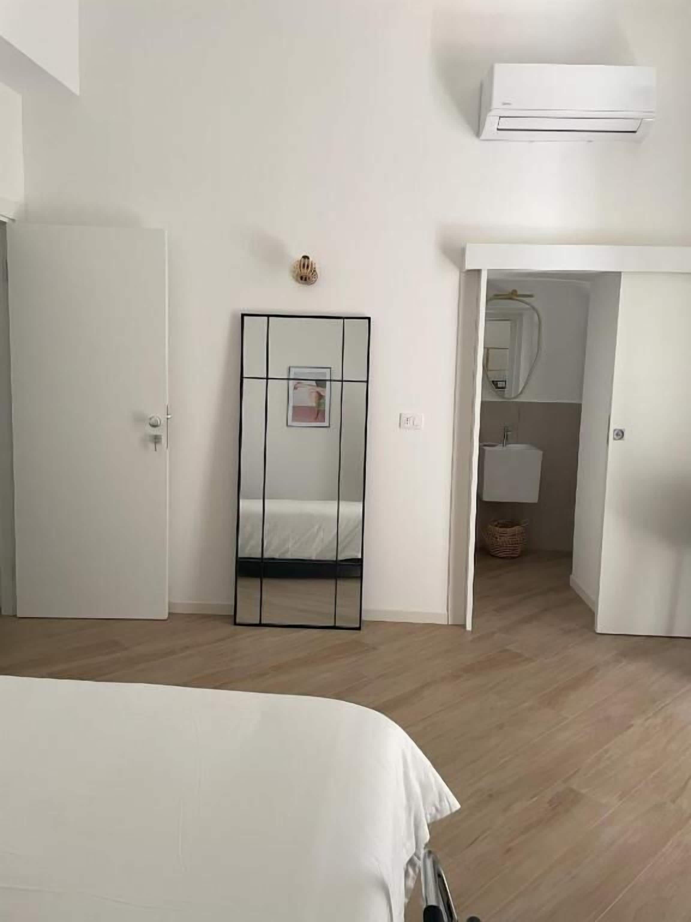 Un dormitorio con cama, espejo, armario y aire acondicionado.