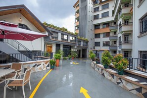 Un edifici de diverses plantes amb terrassa a l'exterior, plantes en testos i un camí ben definit.