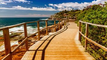 A wooden boardwalk leading to a coastal area with a view of the ocean and a building in the background.