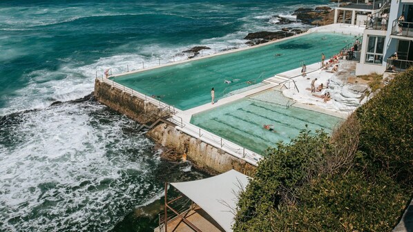 Piscina frente al mar con vistas al océano, una torre de salvavidas y un edificio con balcón.