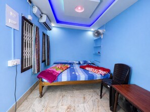 Un dormitorio con cama, escritorio, silla, ventilador de pared y unidad de aire acondicionado.