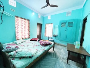 A room with two beds, a ceiling fan, a table with a mug, and a window with curtains. - Radha Krishna Homes - near Sea Beach (Puri)