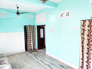A room with teal walls, a ceiling fan, patterned curtains, a door with a mirror, and a tiled floor. - Radha Krishna Homes - near Sea Beach (Puri)