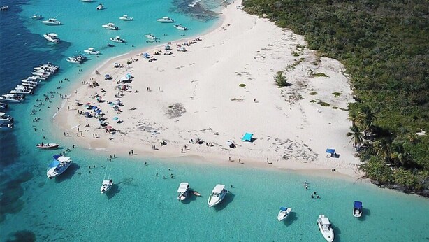 Vista aérea de una playa con barcos, una orilla arenosa y vegetación densa.