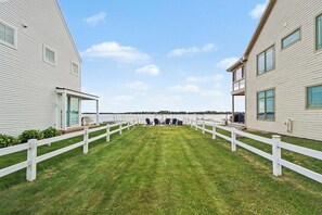 A waterfront property with a grassy lawn, white fences, and two buildings with large windows.